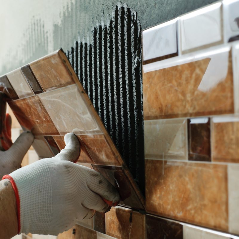 Laying Ceramic Tiles. Tiler placing ceramic wall tile in position over adhesive