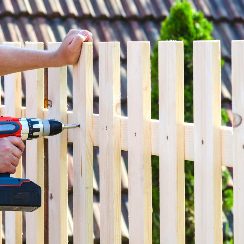 building a wooden fence with a drill and screw. Close up of his hand and the tool in a DIY concept.